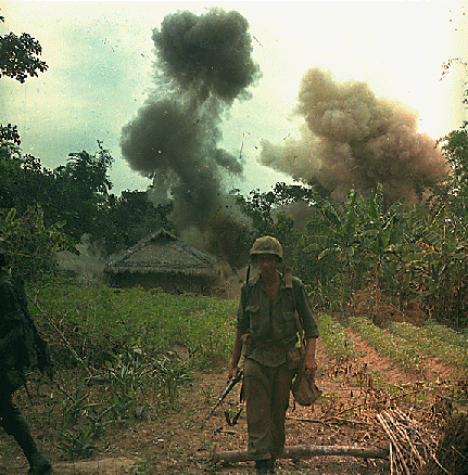 American soldier walking down a path with explosions going on in the background during the Vietnam War.