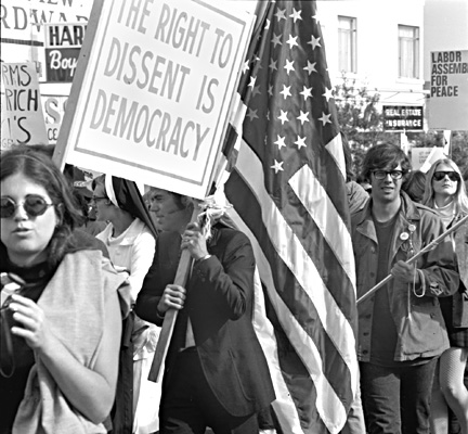 Group of Vietnam War protesters, one man is holding the American flag and a sign that reads "The right to dissent is democracy."